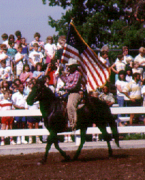 A rider carrying the American flag on a Spanish Barb horse in an arena.